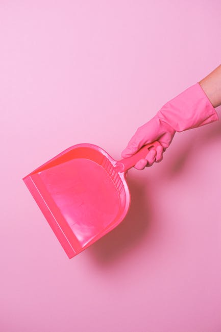 A person wearing a pink rubber glove is holding a pink dustpan against a plain pink background. The dustpan appears clean and unused, with a smooth surface and ridged edge. There are no other visible objects or surfaces in the image. This close-up shot emphasizes the hand and dustpan, illustrating a focus on domestic cleaning tools and hygiene. The scene is well-lit, highlighting the vibrant color of the dustpan and glove, and suggesting a setting associated with thorough surface cleaning and maintenance. Lambeth Carpet Cleaners, as seen on the webpage titled 'Avoid hidden charges in Lambeth cleaning quotes,' promotes professional cleaning services that include surface cleaning and sanitisation, ensuring a clean and hygienic environment.